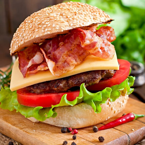 A delicious bacon cheeseburger with lettuce and tomato on a sesame seed bun, served on a wooden board.