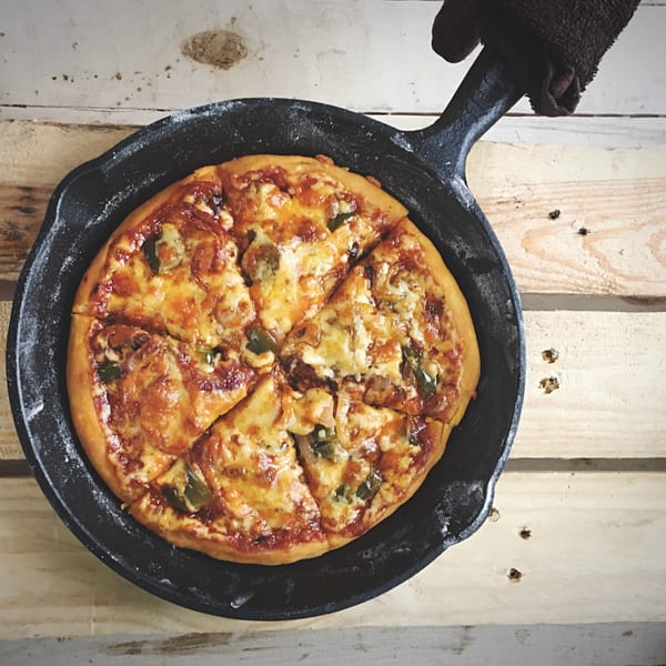 Mike's Pizza Deli Station's hot, sliced pizza with melted cheese and toppings in a cast iron pan.